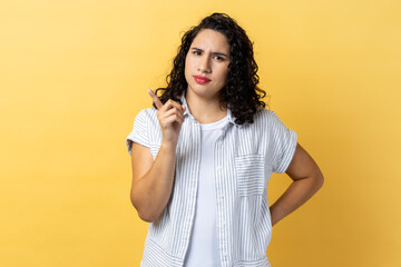 Portrait of serious strict woman with dark wavy hair pointing finger at camera and looking with...