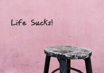 Old chair on grunge pink wall with handwritten text LIFE SUCKS!, saying when things are not going...
