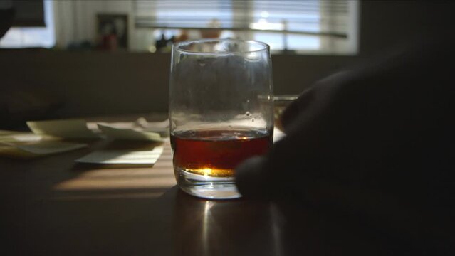 Early morning light and a whiskey glass placed on a living room table with windows in tha background