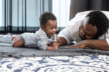 African father and son crawling on the floor, happy father watching his cute baby crawl on floor at home, dad spending time with his cute toddler child, selective focus