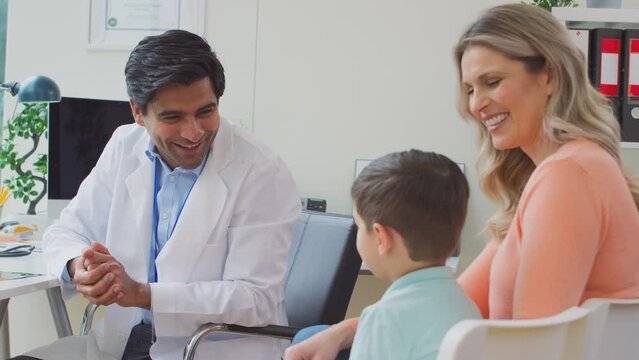Smiling doctor or GP in white coat meeting with mother and son in office for appointment - shot in slow motion