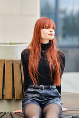 Young woman with red hair sits patiently on bench