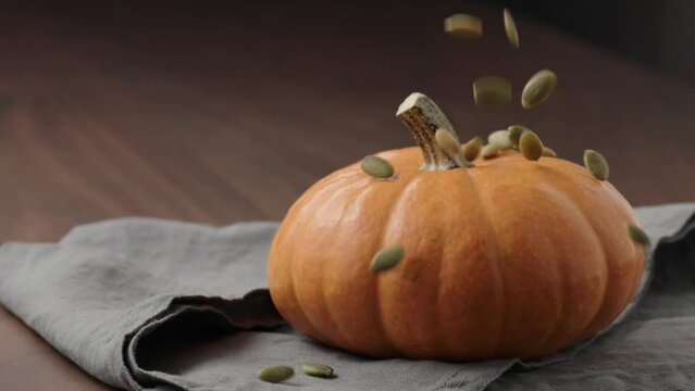 Slow motion pumpkin seeds fall on orange pumpkin on walnut table with linen cloth with copy space