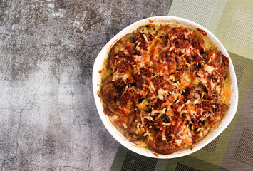 Potatoes Romanoff - potato casserole with cheese and onions in a white baking dish on a dark grey background. Top view, flat lay.