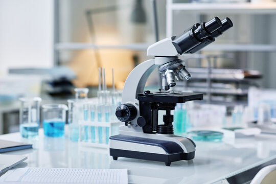 Microscope and group of flasks and other glassware on desk which is workplace of modern scientist carrying out clinical experiment