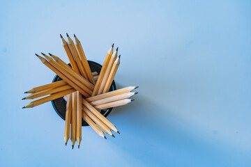 Ordinary graphite pencils in black net pencil cup top view on blue background