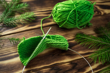 Started knitting on knitting needles, with yarn on a rustic wooden table, with green branches of a Christmas tree.