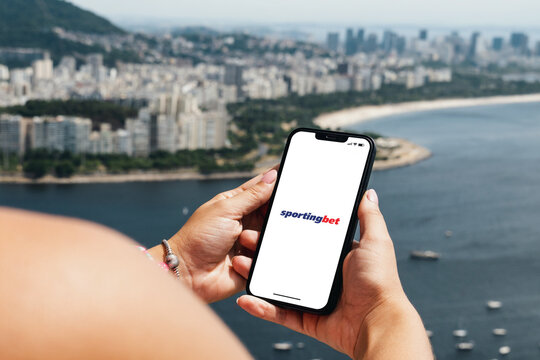 Girl holding smartphone with Sportingbet betting provider app on screen. City and bay with some boats in the background. Rio de Janeiro, RJ, Brazil. November 2022