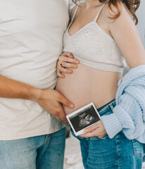 Pregnant woman's belly close-up and printed ultrasound screening. The concept of conscious fatherhood, happy motherhood and easy pregnancy.