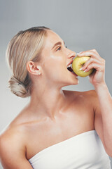 Obraz na płótnie Canvas Nutrition, smile and woman eating an apple for health of teeth, dental and care for body against a grey studio background. Food, diet and happy model thinking of healthy lifestyle with a fruit