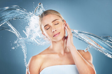 Face, beauty and water splash of woman with eyes closed isolated on a blue background in studio....
