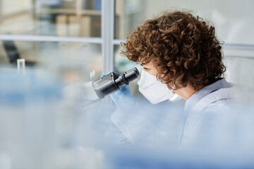 Young woman in respirator carrying out scientific research of new virus while bending over...