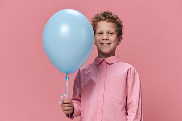 beautiful cute little boy of school age stands with a blue balloon in his hand and poses smiling...