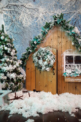 Christmas, New Year hut exterior with garland, fur-tree branches and blue flowers on snow-covered forest background