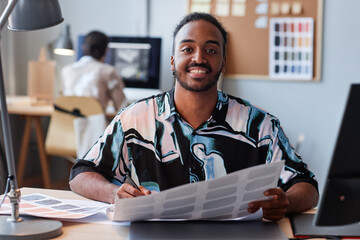 Portrait of smiling Middle Eastern man as creative designer looking at camera and holding color...