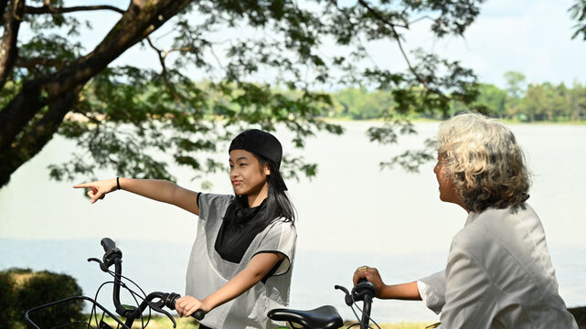 Happy teenage asian girl cycling in summer park on beautiful day with grandmother. Retirement people lifestyle, outdoor activity concept