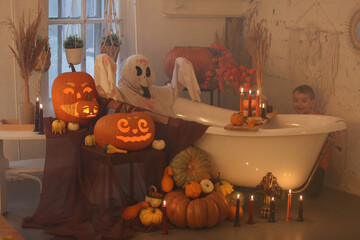 Ghost in bath. Halloween party. Decor with lights, candles and pumpkins. Illuminated pumpkin...