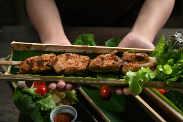 Hands holding bamboo barrel plate with tasty grilled meat. Mala Chinese BBQ is meat or vegetable...