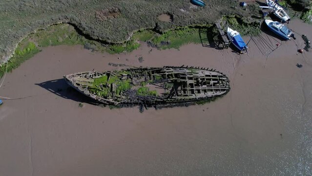Shipwreck Covered With Moss Near Salt Marshes In Tollesbury Marina, Essex, United Kingdom. Aerial Tilt-down
