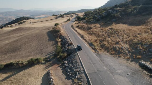 Aerial drone shot over a black car while passing through rural hilly landscape in El Torcal de Antequera, Sierra in Spain during evening time.