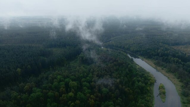 Mystical aerial view of remote river between woods. Low hovering clouds visible. Green environment, high humidity. High quality 4K footage.