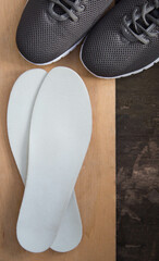 Insoles and sports shoes on old wooden board. Prevention of orthopedic foot diseases, foot care....