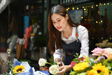 Focused asian female florist wearing apron creating beautiful bouquet with different flowers her floral shop