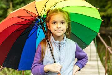 A girl holds a colorful umbrella while walking in the park.