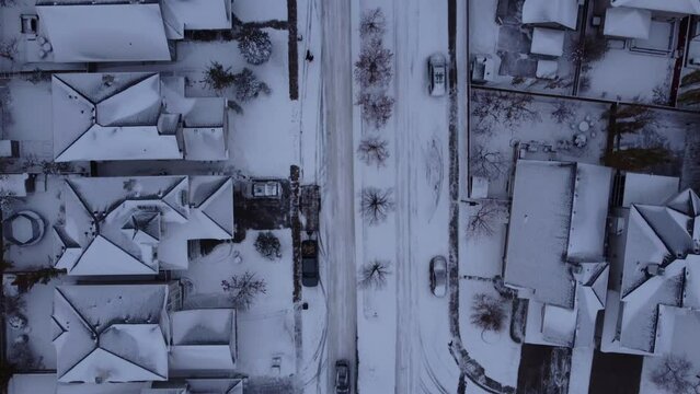 Straight down drone shot over snowy houses with cars driving around