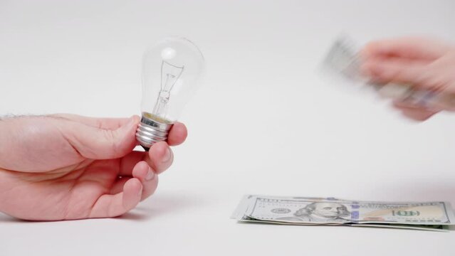 Intellectual property and patent.Man holds electric light bulb, and woman counts out dollar bills on white background.Hands and money close-up.Concept of utility bills and rising energy and electricit