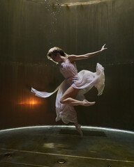 a ballerina dances underwater in a white flowing dress on a dark background in the depths fantasy...