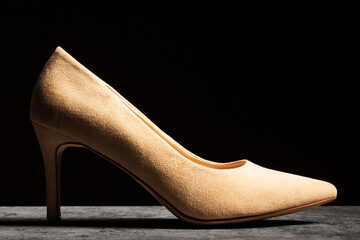 Side view of a beige women's shoe with a heel on a dark background.
