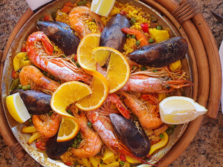 Classic dish of Spain, seafood paella in traditional pan on rustic blue concrete background top view. Spanish paella with shrimps, clamps, mussels, green peas and fresh lemon wedges from above