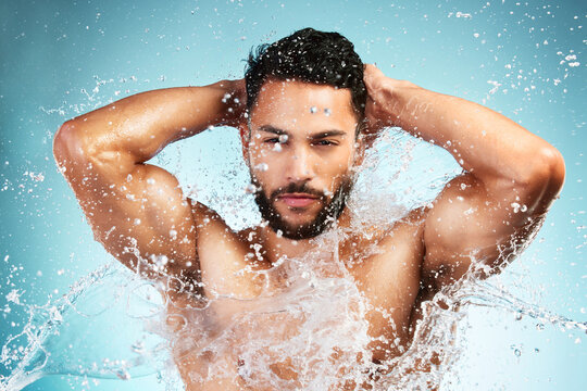 Water, splash and man washing his body on a blue studio background for health and wellness. Bodycare, hygiene and man cleaning or cleansing his body for beauty, wash and clean fresh routine