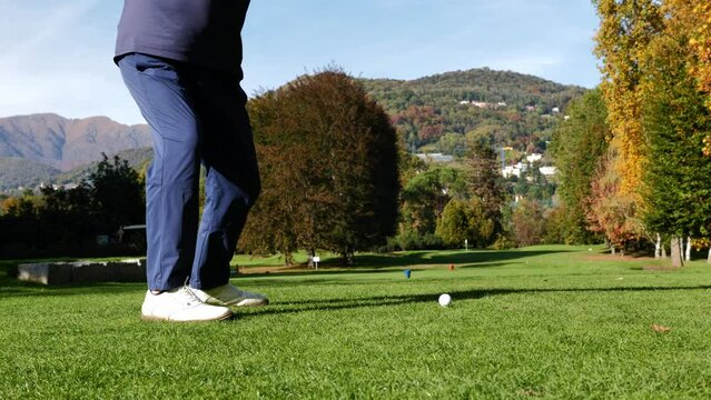 Golfer Teeing Off with His Iron Driver on a Par 3 Hole with Mountain in a Sunny Day in Autumn in Lugano, Ticino, Switzerland.