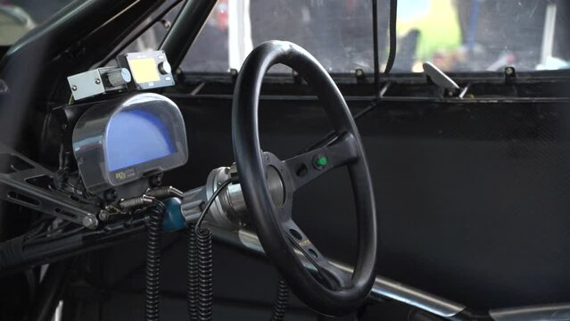 Middle shot of pilot seat inside the real drag racing car with steering wheel and dashboard. Wires, screens and buttons seen also