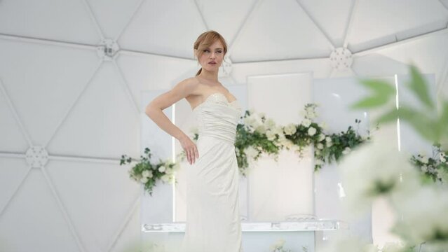 The model poses against the background of the banquet hall. The wedding dress is white. Tent for events.