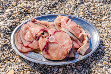 Slices of swordfish ready to be grilled with herbs and pepper on a metal plate on the ground with...