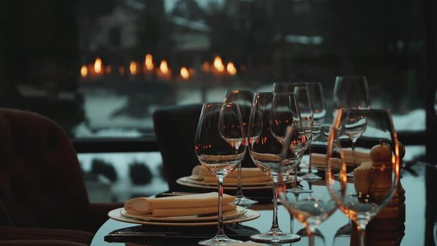 Glass glasses and white plates. Candles are burning in a dark interior of restaurant. The decor of the festive table. The plate is on a black glass table.