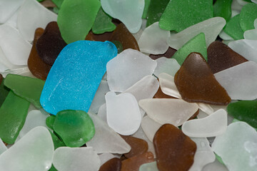 Beach litter - sea glass - worn pieces of broken bottle  - collected from the beach make a colourful display and an attractive wallpaper. A blue piece of sea glass makes an interesting contrast - obrazy, fototapety, plakaty