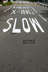 Traffic warning sign painted on the street in a school road. Warning drivers to slow down before passing the crossing area.