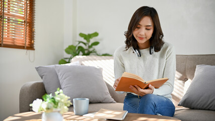Beautiful millennial Asian woman researching some information in textbook, reading a book