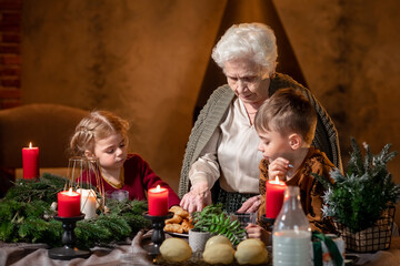Senior old woman grandmother with grandchildren having festive common dinner in Christmas winter time at cosy home with fireplace. Concept family time, relatives and common dinners. New year eve.