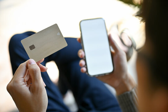 Asian man holding a credit card and his smartphone. phone white screen mockup.
