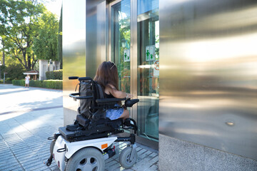 Disabled woman with reduced mobility and small stature in an electric wheelchair trying to enter an...
