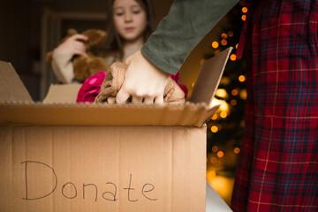 cardboard box with inscription donate. family mother and child put clothes and toys in box at home against background of Christmas tree. donation