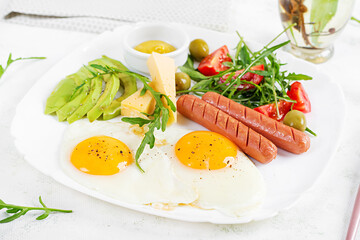 English breakfast - fried eggs, sausages, tomatoes, avocado, cheese and olives. American food.
