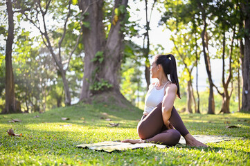 Naklejka na ściany i meble Attractive Asian woman in sportswear doing Half lord of the fished pose, practicing yoga at the park