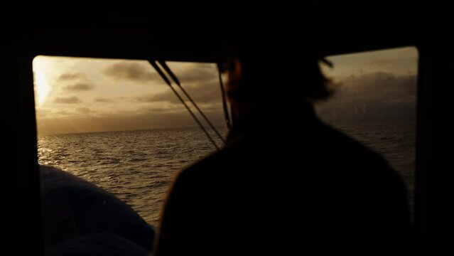 The captain of the ship controls the boat against the backdrop of sunset. The silhouette of a man against the backdrop of a sunset. The water surface is illuminated by the sun. A dramatic sunset with