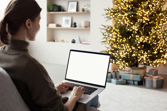 Young woman using laptop computer with blank empty mockup screen during Christmas holidays at home, Online shopping at winter holidays, ordering Christmas gift, Website template